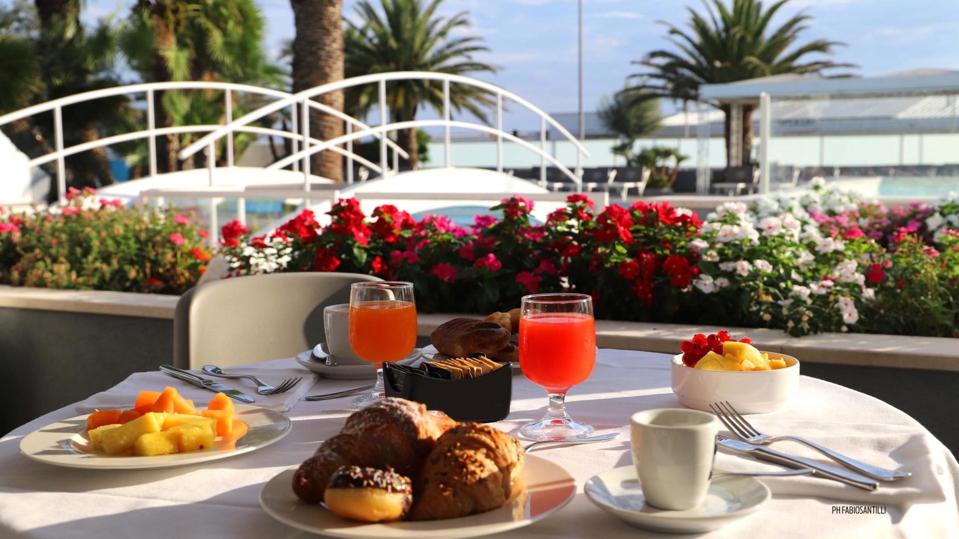 Colazione all'aperto con succhi, frutta e dolci, vista su giardino fiorito.