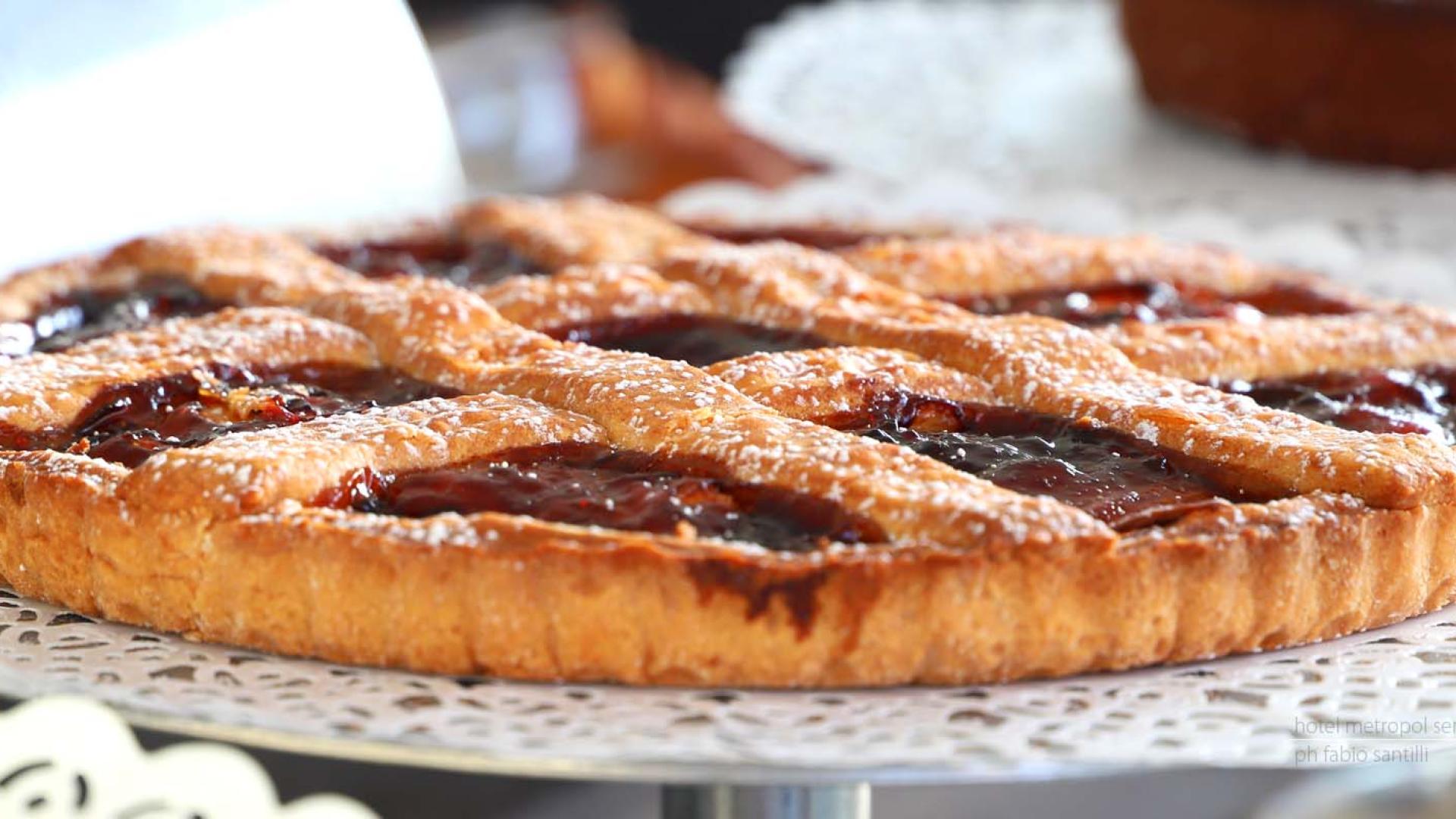 Crostata con marmellata e griglia di pasta frolla, su vassoio decorato.