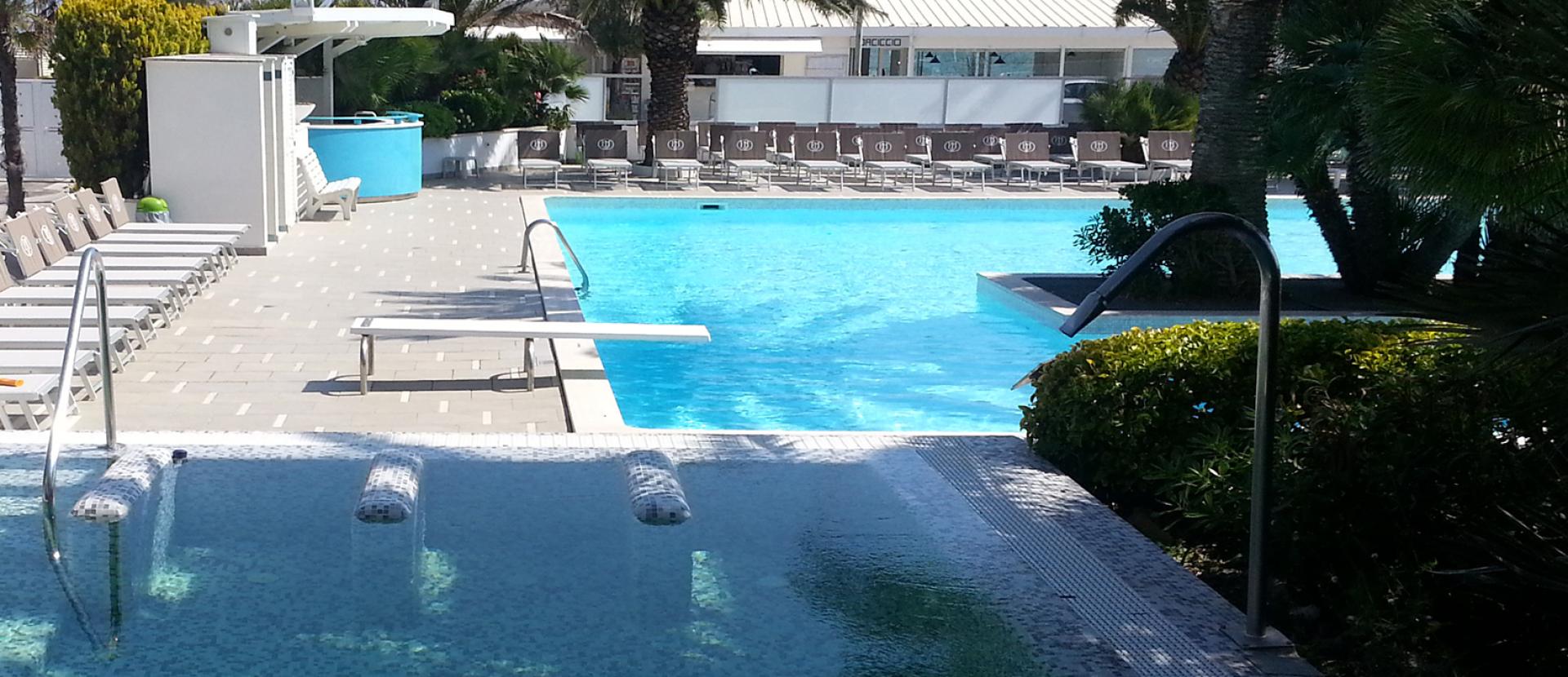 Piscina all'aperto con lettini e palme, atmosfera rilassante e soleggiata.