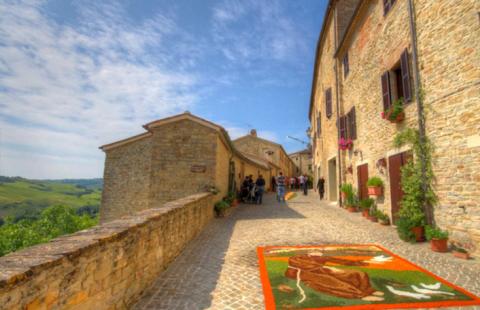 Strada acciottolata con murales floreale, case in pietra e paesaggio collinare.