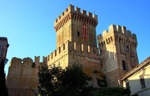 Castello medievale con torri merlate e bandiera, illuminato dalla luce del tramonto.