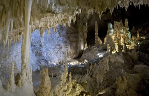 Grotte con stalattiti e stalagmiti illuminate da luci soffuse, creando un'atmosfera magica.