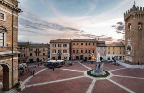 Piazza italiana con torre medievale e statua al centro, al tramonto.