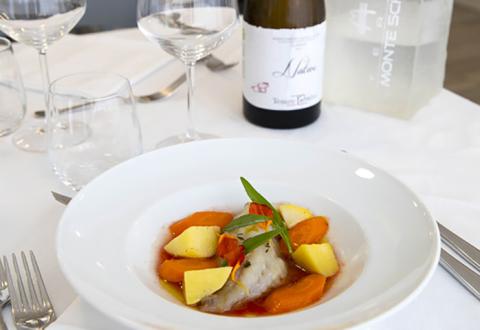 Piatto gourmet con pesce, verdure colorate e vino bianco su tavola elegante.