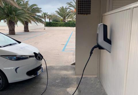 Auto elettrica in carica presso una stazione di ricarica vicino al mare.