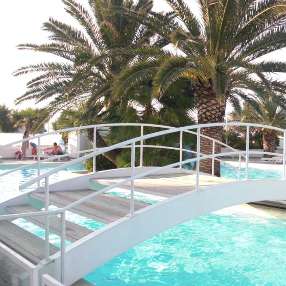 Piscina con ponte bianco e palme, atmosfera rilassante e soleggiata.