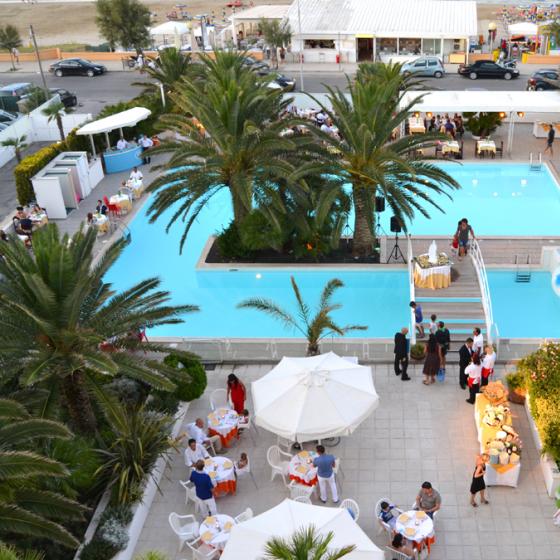 Piscina all'aperto con palme, tavoli per cena e vista sulla spiaggia.