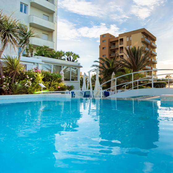 Piscina all'aperto con palme e edifici sullo sfondo al tramonto.