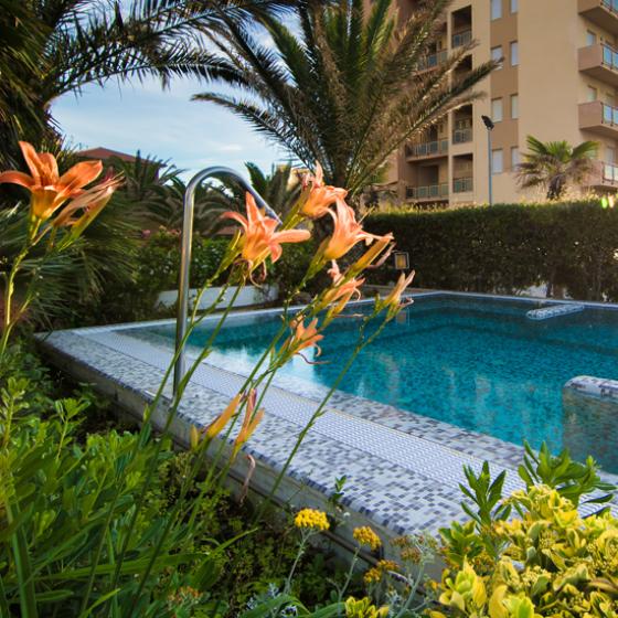 Piscina con mosaico e fiori, edificio sullo sfondo al tramonto.