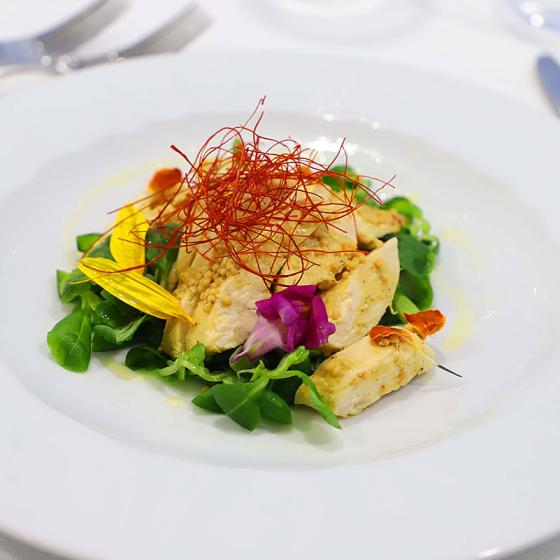 Insalata di pollo con verdure fresche e decorazioni floreali su piatto bianco.