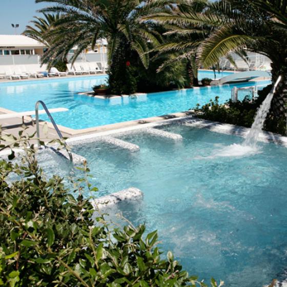 Piscina con idromassaggio circondata da palme e lettini per il relax.