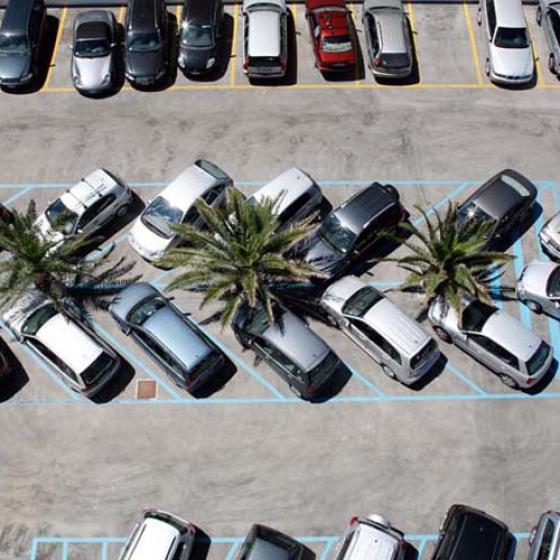 Parcheggio con auto disordinate tra palme, vista dall'alto.