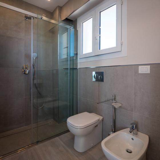 Bagno moderno con doccia in vetro, WC e bidet, pavimento e pareti in grigio.