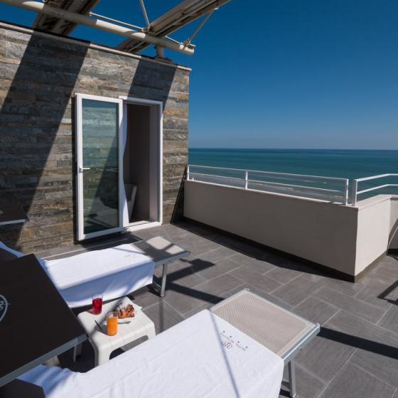 Terrazza con lettini, vista mare, bevande e cielo sereno.