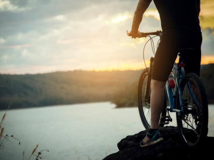 Ciclista su una scogliera al tramonto, osservando il panorama sul lago.