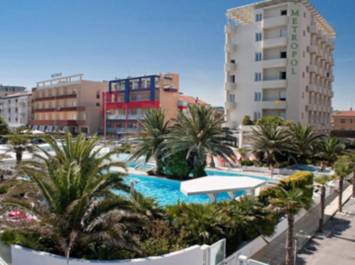 Hotel con piscina, palme e vista sulla città, ambiente moderno e soleggiato.