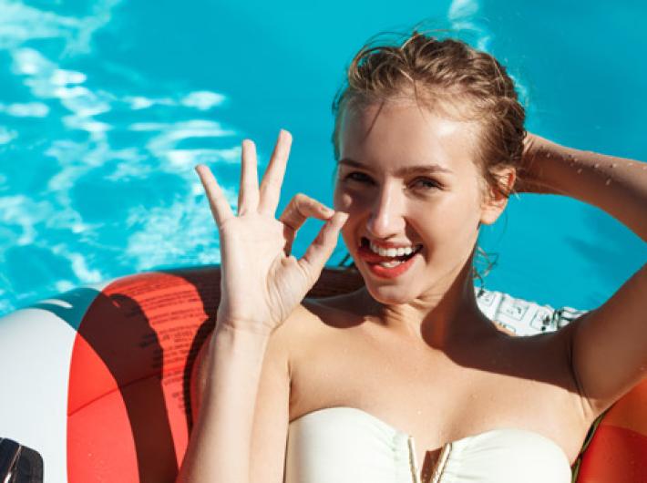 Donna sorridente in piscina, fa il gesto OK con la mano.